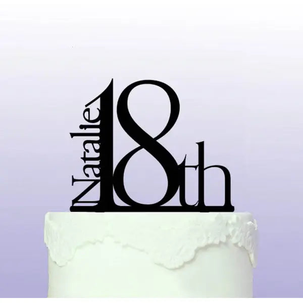 A black cake topper featuring the name &quot;Natalie&quot; and the number &quot;18th,&quot; positioned on a white frosted cake. The design is modern and elegant, against a soft purple background.