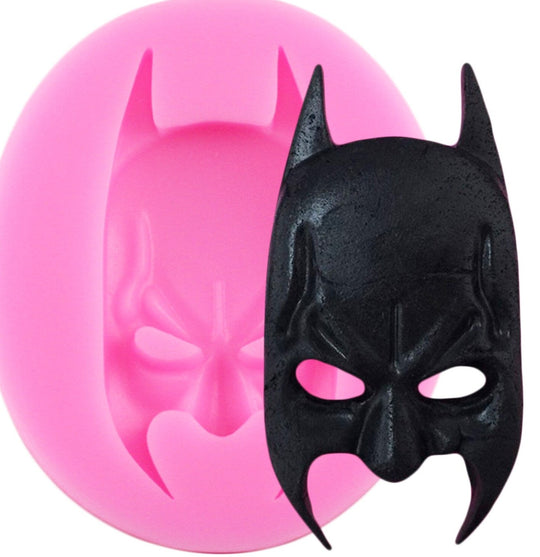 An image showing a pink silicone mold shaped like a batman face, with the completed black batman face figurine placed beside it. The mold features detailed contours and the batman emblematic ears, while the figurine has a textured surface, replicating the design of the mold.