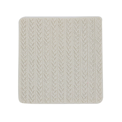 A square silicone mold with a textured surface resembling a knitted pattern. The mold is off-white in color and features raised lines and shapes that mimic the appearance of knit stitches.