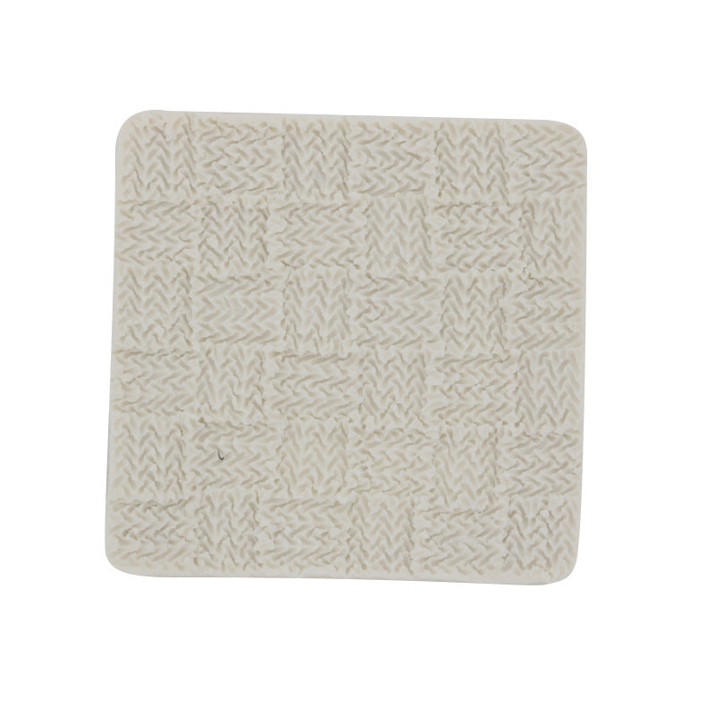 A square silicone mold with a textured surface resembling a knitted pattern. The mold is light-colored and features small squares with intricate stitching details, suggesting a cozy, knit fabric design.