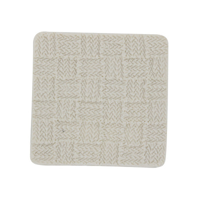 A square silicone mold with a textured surface resembling a knitted pattern. The mold is light-colored and features small squares with intricate stitching details, suggesting a cozy, knit fabric design.
