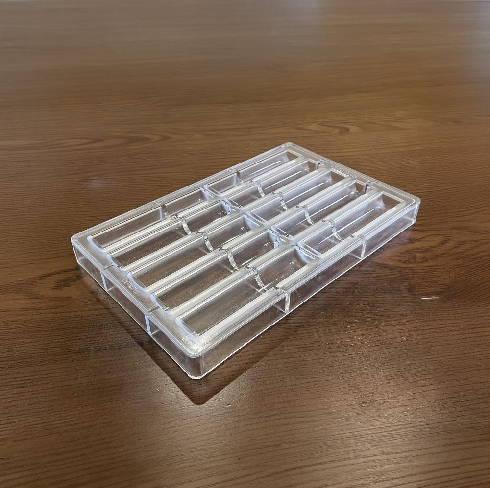 Clear, rectangular ice cube tray with empty slots on a wooden surface. The simple design and warm tone convey functionality and everyday use.