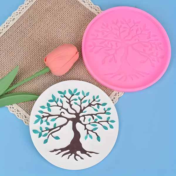 A round pink silicone mold featuring an intricate tree design with branches and leaves. The image also includes a completed fondant decoration of a tree with green leaves on a white background, showcasing the mold&