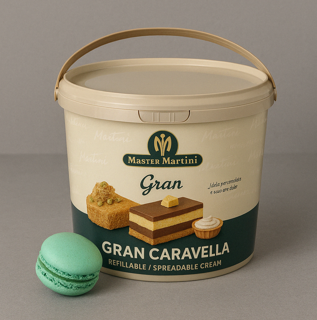 A beige bucket labeled "Master Martini Gran Caravella" with cake and cream images on it, sits against a gray background next to a green macaron.