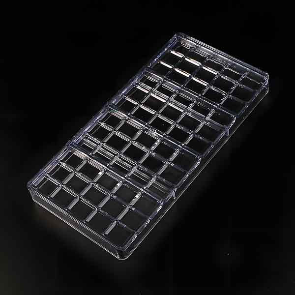 A clear plastic mould designed for making four small chocolate bars. The mould features a grid pattern with multiple rectangular cavities, each suitable for shaping individual chocolate bars. The background is black, which highlights the clarity and shape of the mould.