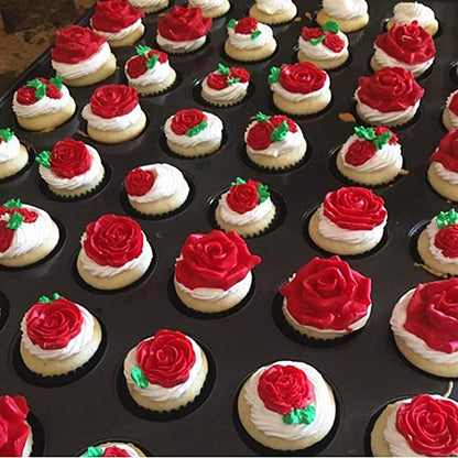 A tray filled with decorative cupcakes, each topped with frosting and detailed floral designs. The cupcakes feature vibrant red roses made from icing, some accompanied by green leaves and additional small red accents. The arrangement showcases a variety of decorated cupcakes, combining smooth white frosting with the bright red rose designs.