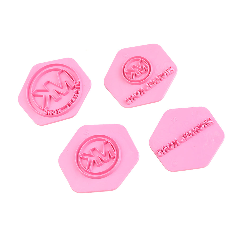 A set of four pink hexagonal fondant embosser cutters featuring the initials &quot;MK&quot; and the text &quot;MICHAEL KORS&quot; imprinted on the surface. The cutters vary slightly in design but maintain a cohesive look with a rounded center and edges.