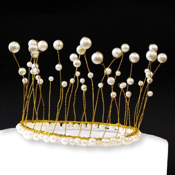 A decorative cake topper designed as a crown, featuring a gold wire base adorned with clusters of pearl-like beads. The crown has an open design with varying heights of wire that mimic the spikes of a traditional crown, embellished with white pearls of different sizes. The topper sits on a white cake, and the background is black, enhancing the visual contrast.