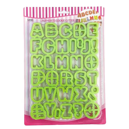 The image shows a packaging of plastic alphabet cookie cutters. The cookie cutters are shaped like letters and symbols from A to Z, including an exclamation mark and a question mark. They are bright green in color and are arranged neatly in the package. The packaging features a pink striped border at the top, with the words "Alphabets Cookie Cutter" displayed prominently. The overall design is colorful and playful, suitable for baking and decorating cookies.