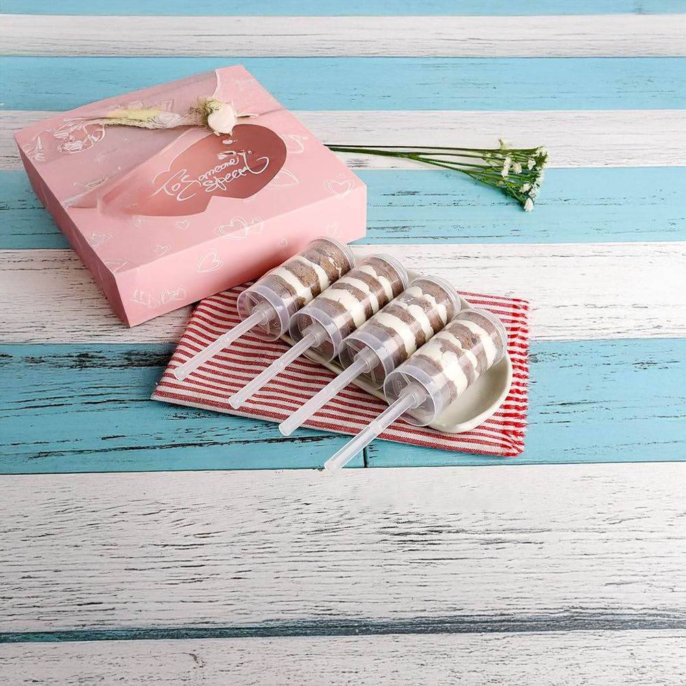 Three lollipops with striped sticks on a red and white checkered cloth next to a pink gift box on a blue wooden surface.