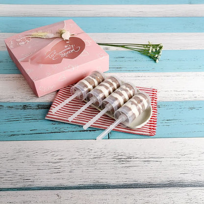 Three lollipops with striped sticks on a red and white checkered cloth next to a pink gift box on a blue wooden surface.