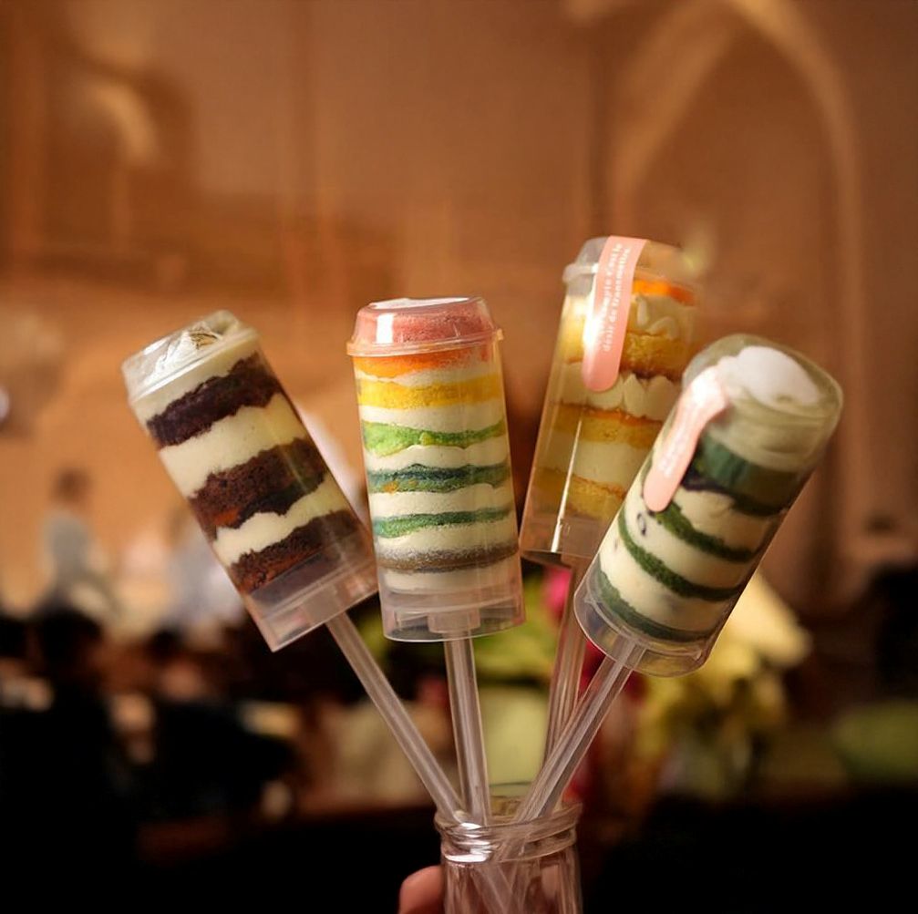 Colorful layered cake pops held together with a clear ribbon against a blurred indoor background.