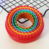 A round cookie cutter set consisting of six nested cutters in various colors. The outer cutter is red, followed by yellow, orange, green, light blue, and dark blue. The cutters are sitting on a light surface with a black wire cooling rack in the background.