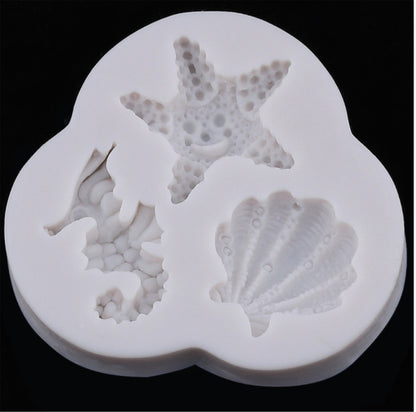 The image shows a white silicone mold designed for creating decorative shapes. The mold features three cavities in the shapes of a seahorse, a starfish, and a shell. Each design has detailed textures, representing realistic features of each marine creature. The mold is rounded and has a smooth finish, suitable for baking or crafting purposes. The background is black, highlighting the white silicone material of the mold.