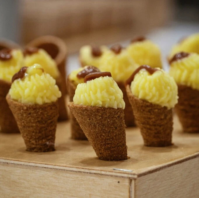 A wooden tray displays an assortment of ice cream cones, each topped with different vibrant flavors.