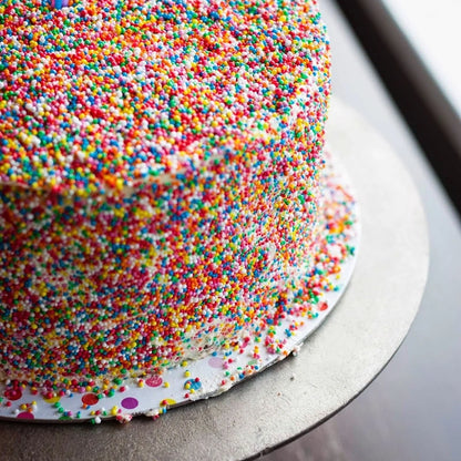 Close-up of a cake covered in colorful sprinkles on a metal surface.