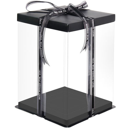 A square tall cake box made of clear PVC material with a black base. The box is topped with a black lid and features decorative ribbons that read "BEST WISHES FOR YOU." The box is displayed with an open design, highlighting its spacious interior.