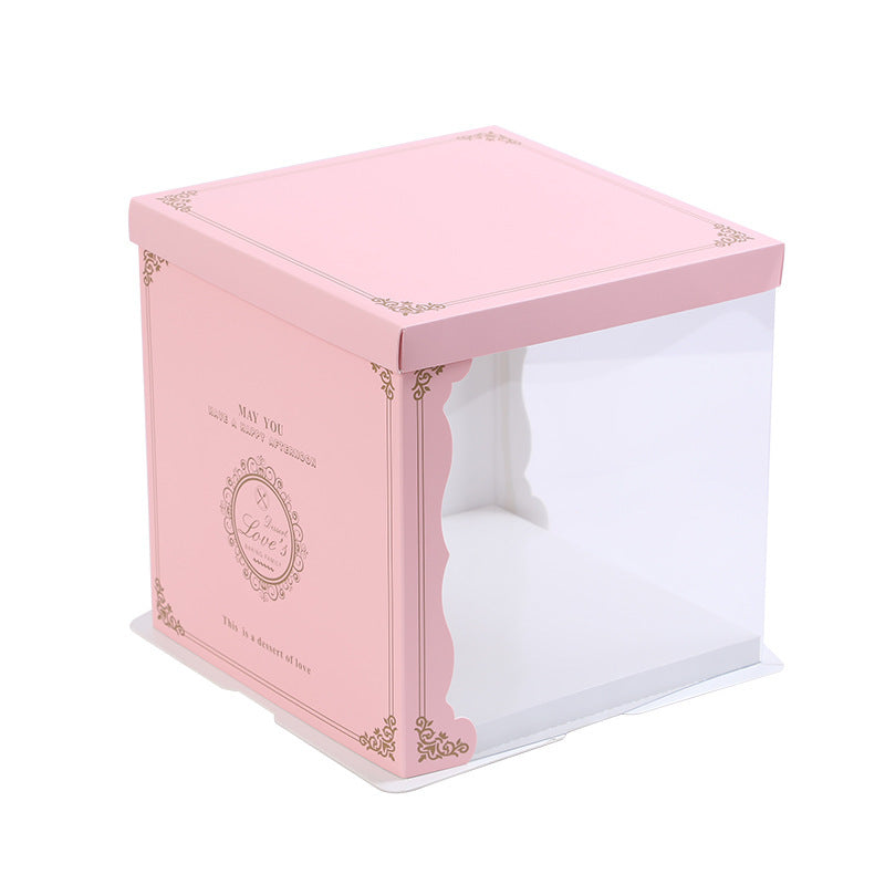 A square cake box with dimensions 12 x 12 x 14 inches. The box features a pink exterior with decorative gold accents and text that reads &quot;MAY YOU&quot; and &quot;This is a dessert of love.&quot; The front side of the box is transparent, allowing a view of the contents inside.