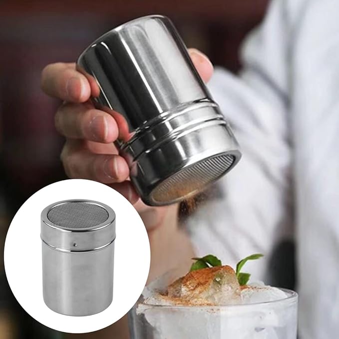 A hand holds a stainless steel shaker, dusting powder over a dessert with mint garnish. Inset shows a close-up of the shaker. Elegant and precise.
