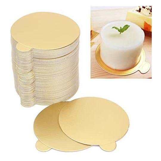 Image shows a stack of round, gold mini cake boards, each measuring 10 cm in diameter. Two boards are placed in the foreground, highlighting their shiny finish. In the background, a small cake is displayed on a matching gold board, featuring a mint leaf on top. The setting appears to be a wooden surface.