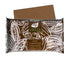 A 2.5 kg package of Virtue milk chocolate compound. The packaging features a brown background with white cocoa bean illustrations. The product name "VIRTUE" is displayed prominently in green, along with the text "MILK COMPOUND CHOCOLATE" in white. There are also labels indicating "PREMIUM," "QUALITY," and "GUARANTEED." An additional piece of chocolate can be seen partially above the package.