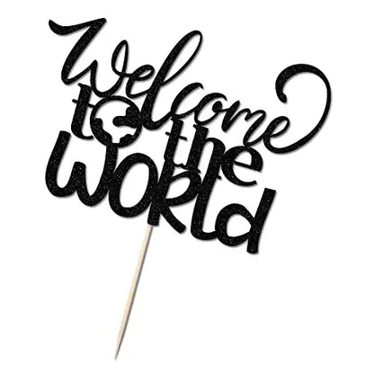A black cardstock cake topper featuring the phrase "Welcome to the World" in a decorative, cursive font. The words are artistically arranged, with a small globe graphic integrated into the text. The topper is attached to a wooden stick for easy placement on a cake. The overall design has a sparkly appearance.