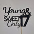 The image features a cake topper made of black glitter cardstock. The design includes the phrases "Young & Sweet" in a flowing script font, with "Only" in a bold, capitalized font. The number "17" is prominently displayed, also in a bold font, indicating a celebration for a 17th birthday. The topper is mounted on a stick for easy placement on a cake, and it is set against a plain background.