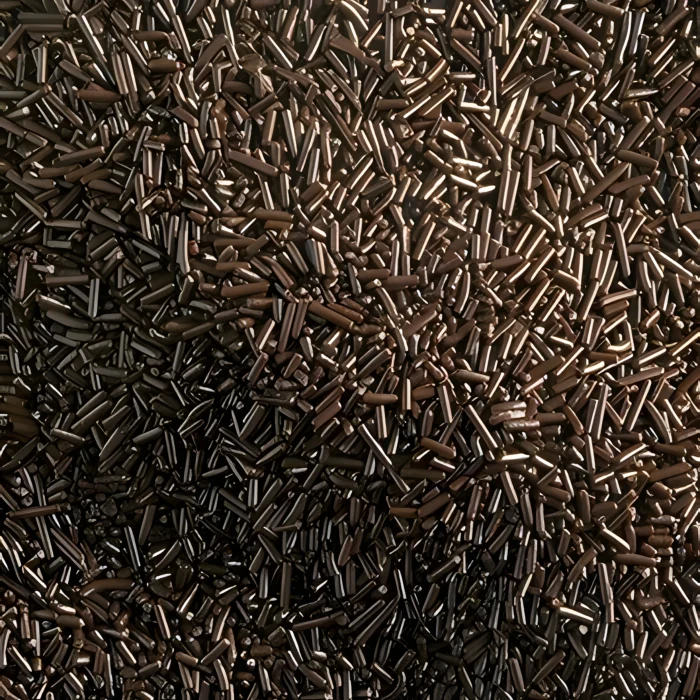 A close-up view of thin, elongated dark chocolate sprinkles or vermicelli strands forming an intricate textured pattern.